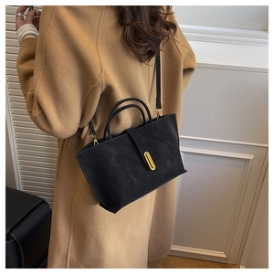 Detail of a large black matte tote bag with gold metal clasp on a model's shoulder