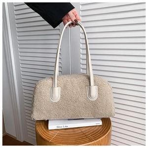 Détail d'un sac à main beige en peluche avec anses en cuir crème posé sur un livre