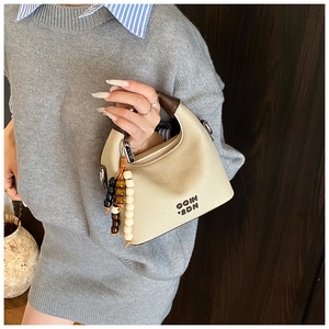 Close-up of cream leather handbag with beaded charm and dark brown top handle details