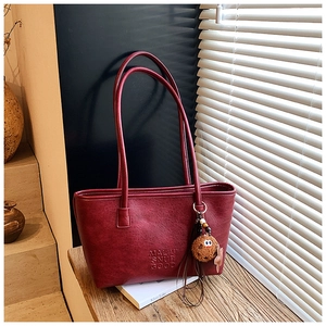 Détail d'un sac cabas vintage bordeaux avec texte embossé et pendentif ours en peluche