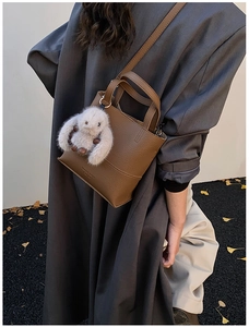Brown litchi grain leather bucket bag with cute plush bunny charm on a casual shoulder strap
