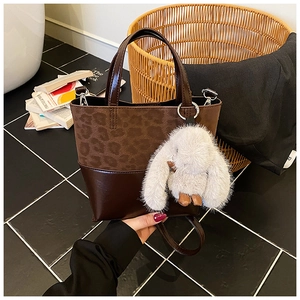 Detail of leopard print tote bag with brown leather bottom and white bunny plush charm