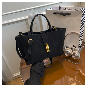 Detail of a black matte tote bag with gold metal clasp and adjustable strap on a desk