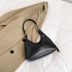 Glossy black crescent shoulder bag with white lettering detail on camel coat background
