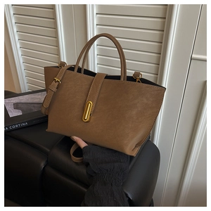 Detail of a brown tote bag featuring a gold oval metal clasp and smooth matte leather texture