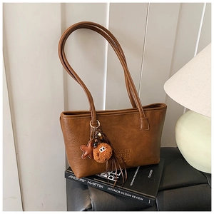 Détail d'un sac cabas en cuir marron avec texte embossé et pendentifs en peluche sur livres