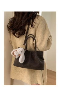 Sac baguette en daim marron foncé avec un charmant lapin en peluche sur un manteau beige