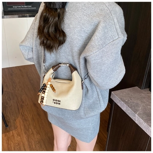Chic beige tote bag with dark brown circular handles and vintage beaded charm detail