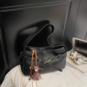 Détail du sac bandoulière en cuir noir avec boucle dorée et breloque ours marron