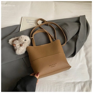 Close-up of brown textured leather bucket bag with a white plush rabbit pendant and handle
