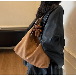 Detail of a large brown suede tote bag featuring a plush bear charm and white printed text