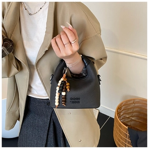Close-up of black pebble-grain handbag featuring wood bead charm and embossed lettering
