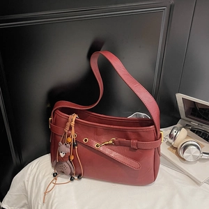 Détail d'un sac bandoulière rétro en cuir bordeaux avec boucle dorée et petit ours