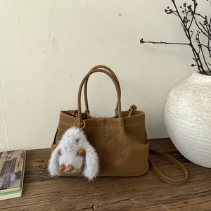 Détail du sac seau en daim marron avec un porte-clés lapin en peluche sur table en bois
