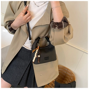 Detail of black lychee leather crossbody bag with wooden bead tassel and engraved COIH logo