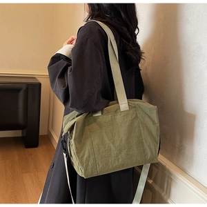 Olive green tote bag with grey straps shown on shoulder in a minimalist indoor setting