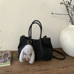 Détail d'un sac seau en daim noir avec un porte-clés lapin en peluche sur table en bois