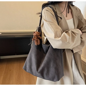 Charcoal grey suede tote bag with brown bear charm worn with a beige trench coat