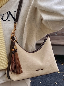 Minimalist beige suede underarm shoulder bag with brown tassels and metallic ring accents