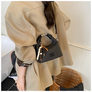 Detail of black leather handbag featuring bead charm and crossbody strap on casual outfit