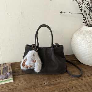 Détail du sac seau en daim marron foncé avec un porte-clés lapin en peluche blanc sur bois