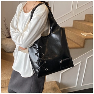 Detail view of black glossy PU leather tote bag with stylish criss-cross lace-up design