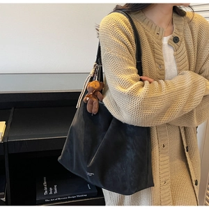 Detail of a black suede tote bag with a brown plush bear charm and white printed text