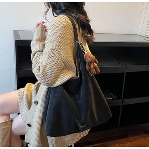 Detail of black tote bag with white stitching, plush bear charm, and large capacity style