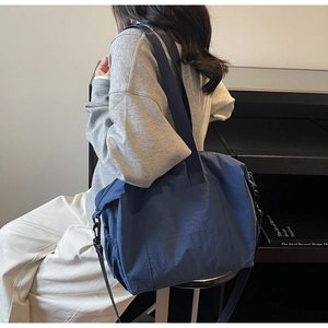 Detail of a large navy nylon tote bag with side drawstring pockets and adjustable strap