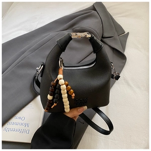 Detail of black lychee grain leather handbag with wood bead charm and silver buckle strap