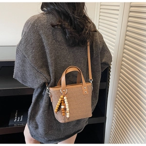 Dettaglio di una borsa a secchiello intrecciata marrone scuro con ciondolo in legno e tracolla