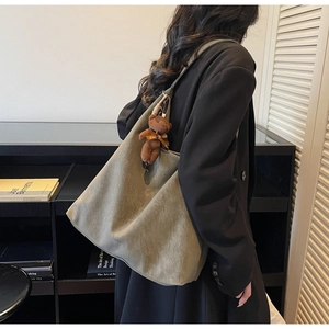 Detail of olive green suede tote bag with a cute plush bear charm on a model's shoulder