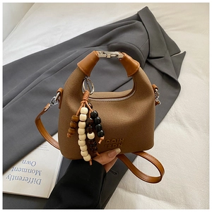 Detail of brown leather bag featuring wood bead tassel and silver clasp closure