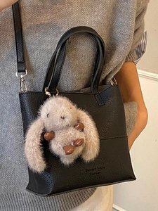 Minimalist black pebbled leather bucket bag with cute grey plush rabbit charm accessory