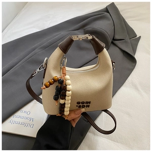 Detail of woven square handbag with brown leather trim and decorative beaded tassel