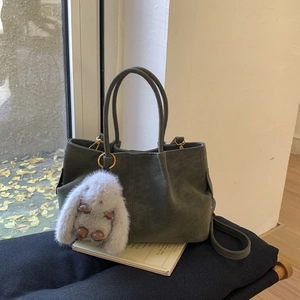 Détail d'un sac seau vert olive avec un charm lapin en peluche dans un décor automnal