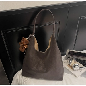 Detail of dark brown suede Hobo bag with plush bear charm and sleek laptop bag lifestyle