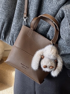 Brown litchi grain leather bucket bag with plush rabbit charm and shoulder strap