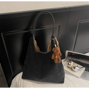 Detail of black suede tote bag featuring white contrast stitching and brown bear charm