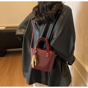 Dettaglio borsa a mano intrecciata rosso scuro con nappa di perline su giacca