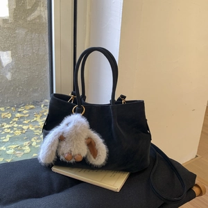 Détail d'un sac seau en daim noir avec un charm lapin à poils longs sur un siège