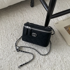 Detailed macro view of black quilted vanity bag with silver metal logo and chain strap