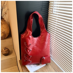 Detail of red PU leather tote bag with silver lace-up decor on a wooden desk