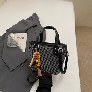 Dettaglio della borsa a secchiello intrecciata con finiture in pelle e nappa di perline in legno