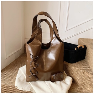 Close-up of a glossy dark brown tote bag with lacing detail and decorative zipper pocket