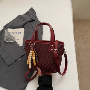 Dettaglio di una borsa a mano intrecciata bordeaux con nappa in perline di legno e manico