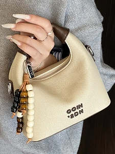 Beige canvas crescent handbag with brown leather handles and wooden bead pendant details