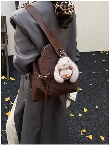 Detail of a brown bucket bag with pleated texture and a plush bunny charm in an autumn setting