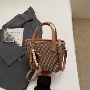 Dettaglio della borsa a secchiello in paglia intrecciata con manici in pelle e perline