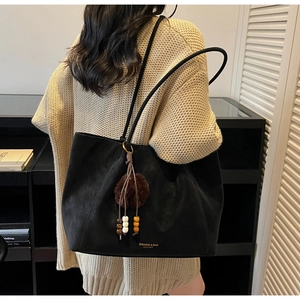 Detail of black suede tote bag with plush charm and brand logo against home decor